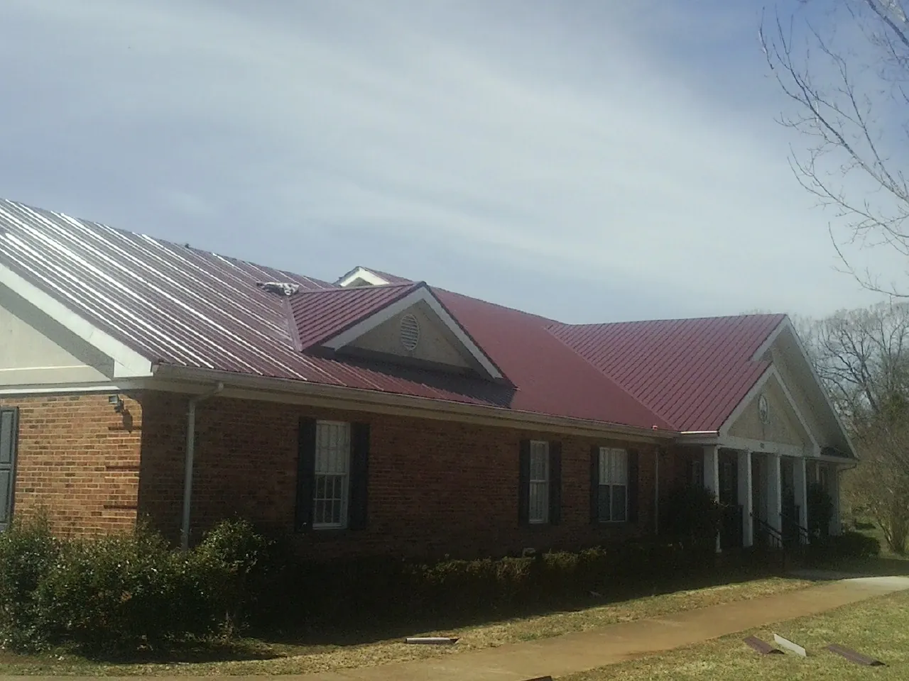 Red metal roof with gabled entries on a long brick building, from a Hail Damage Roof Repair job in Kersey