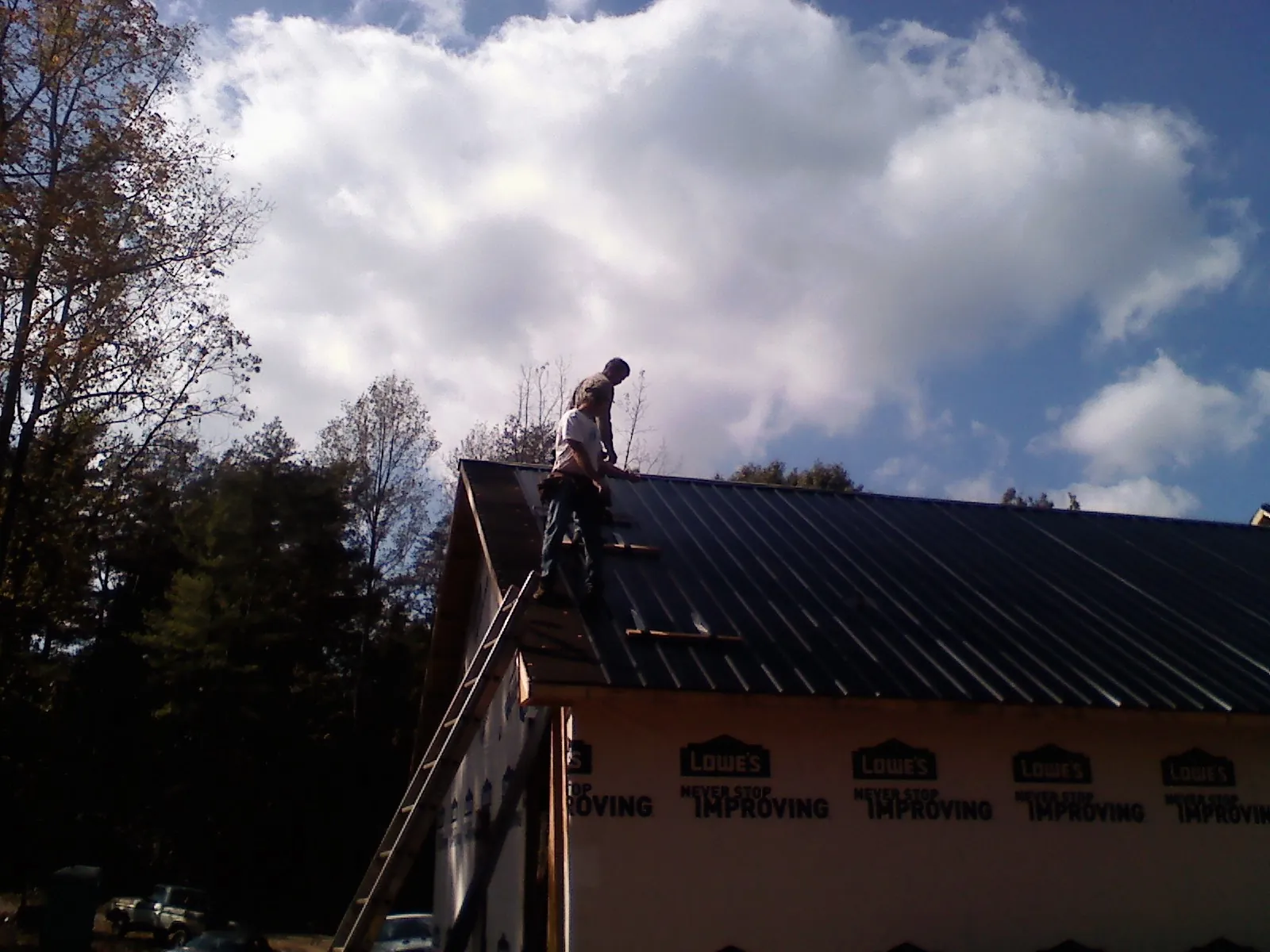 Roofer fastening dark metal panels high against a cloudy sky, from a Roof Inspection job in Kersey