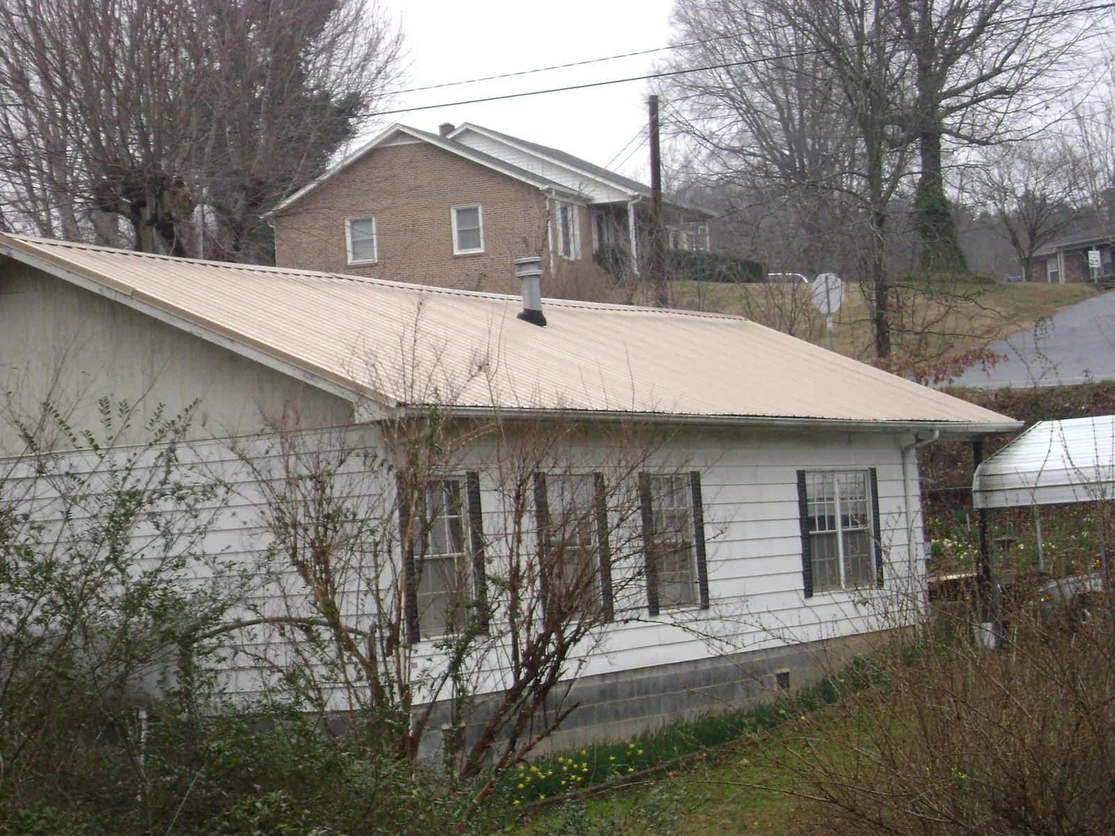 Tan metal roof on a white sided house set into a hillside — Commercial Roofing by Roofing Brothers in Kersey