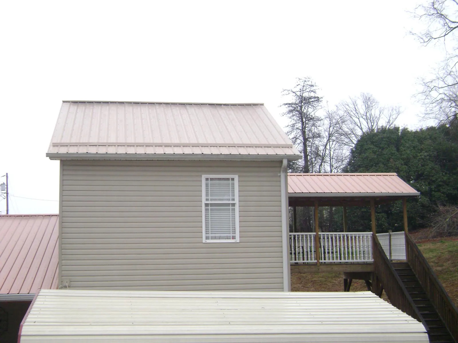 Tan metal roofs on a two story addition and attached porch, from a Roof Replacement job in Kersey